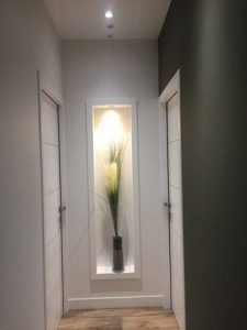 Image représentant une fin de couloir éclairé et des portes de chaque côtés, avec une plante incrusté dans le mur